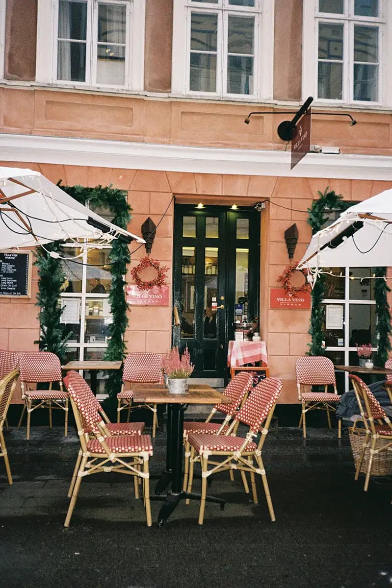 En terrasse med flere stole og parasoller, med udsigt til gaden og bygninger i baggrunden, der skaber en hyggelig udendørs spiseatmosfære.